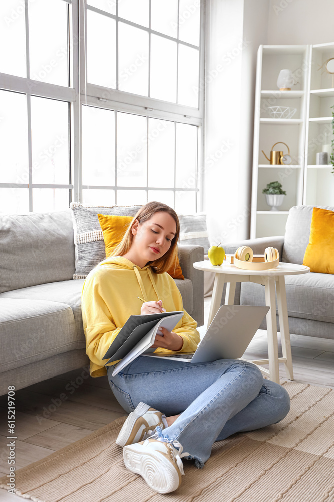 Female student studying with notebook and laptop at home