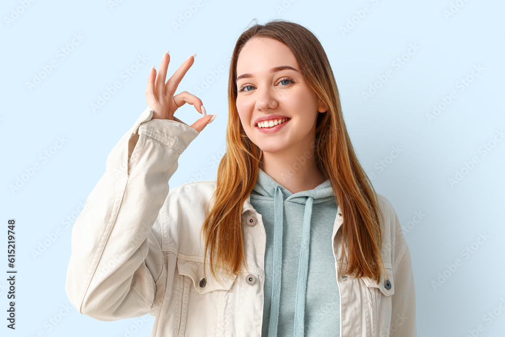 Beautiful young woman showing OK on blue background