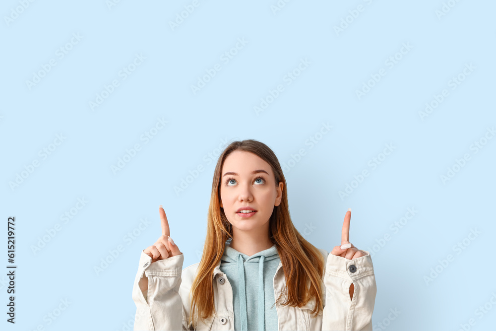 Beautiful young woman pointing at something on blue background