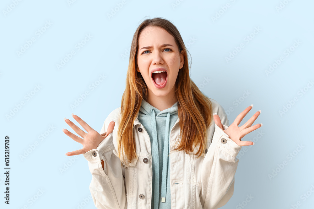 Angry young woman shouting on blue background