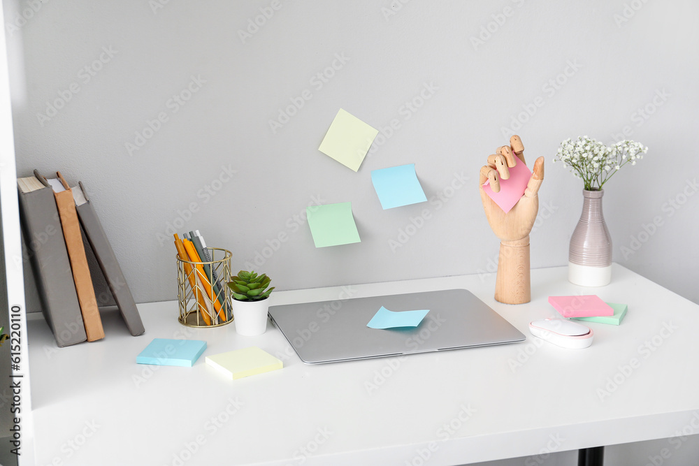 Wooden hand with sticky notes and laptop on table near light wall