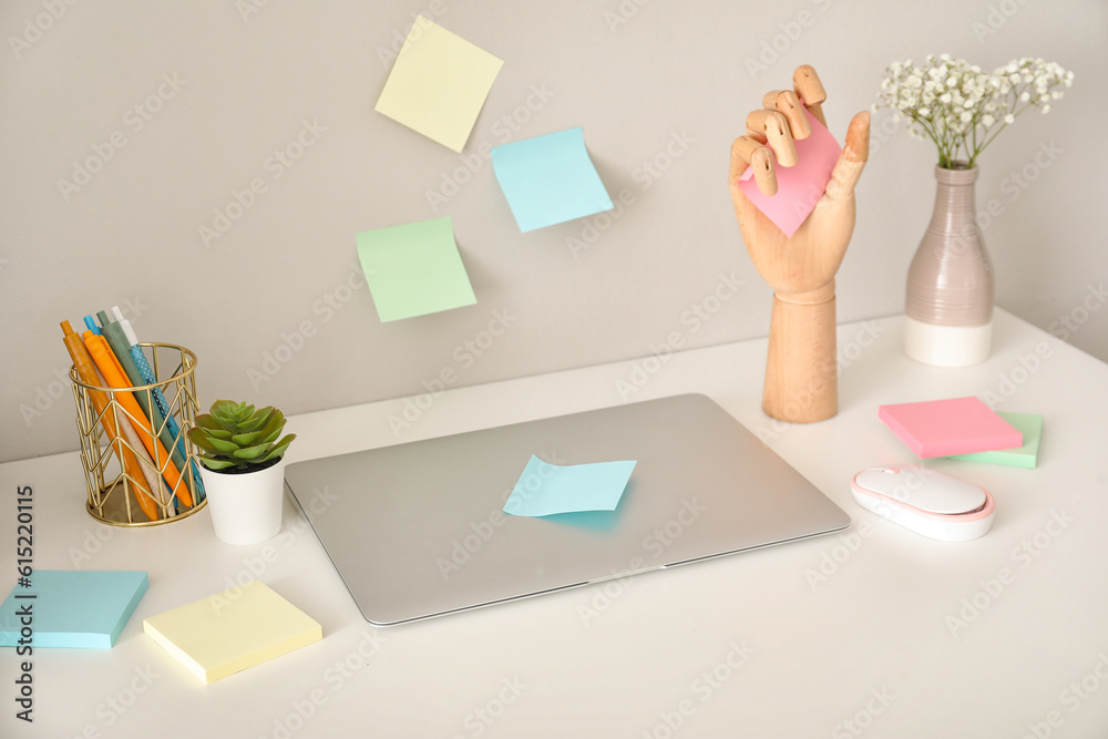 Wooden hand with sticky notes and laptop on table near light wall