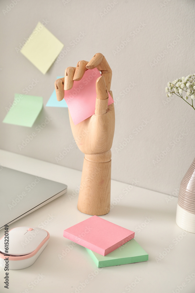 Wooden hand with sticky notes and laptop on table near light wall