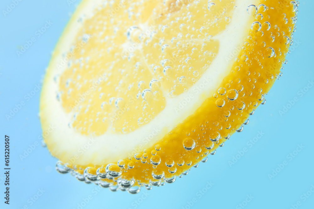 Lemon slice in water with bubbles on blue background