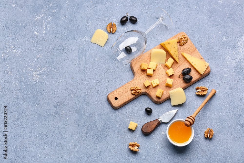 Wooden board with pieces of tasty cheese, wine glass and honey on grey background