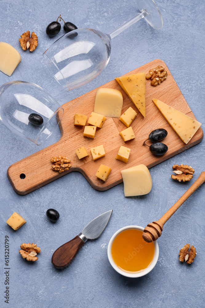 Wooden board with pieces of tasty cheese, wine glasses and honey on grey background