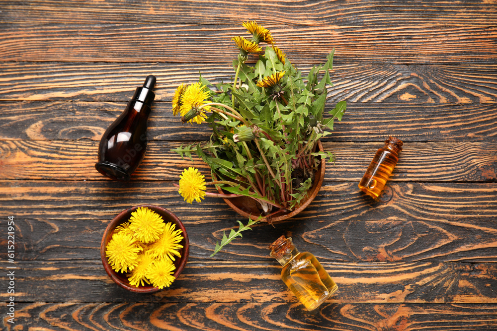 Bottles with cosmetic oil and bowls of dandelion flowers on wooden background