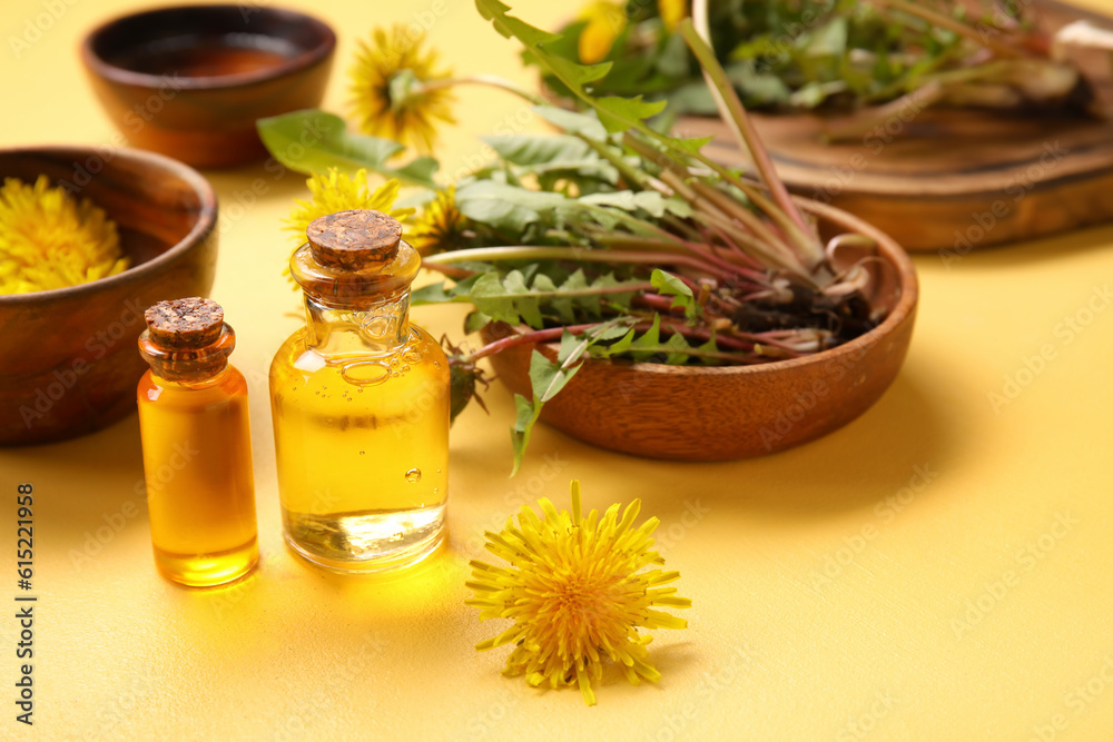 Bottles with cosmetic oil and bowls of dandelion flowers on yellow background