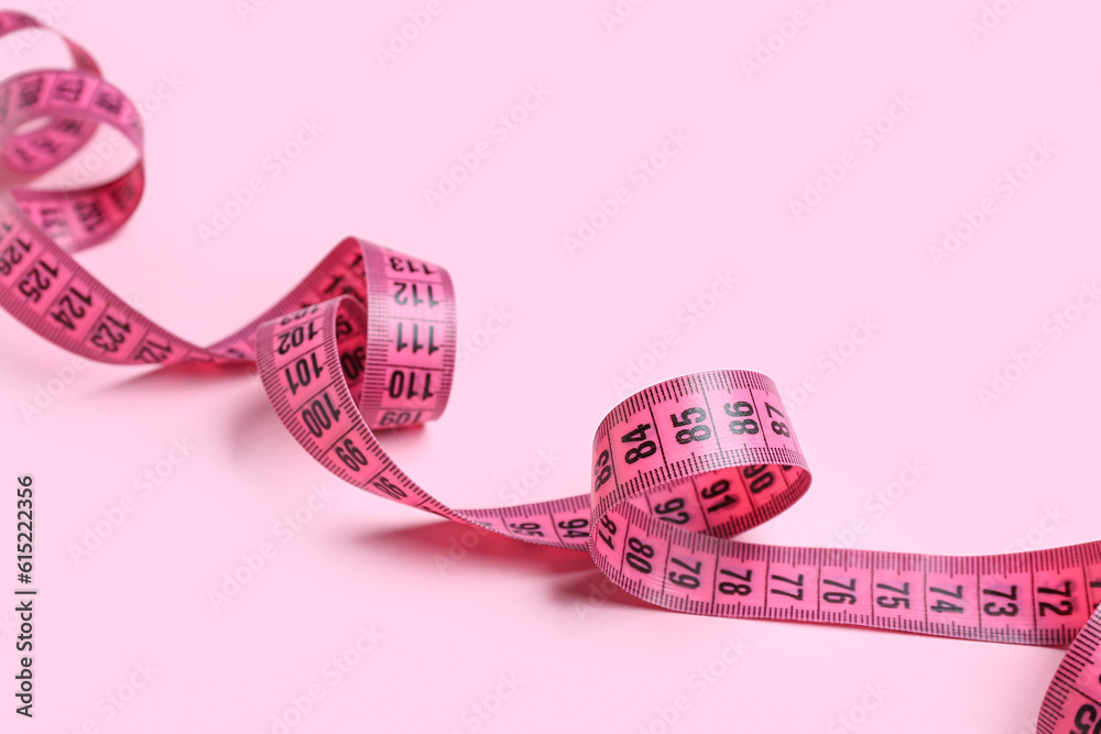 Measuring tape on pink background, closeup