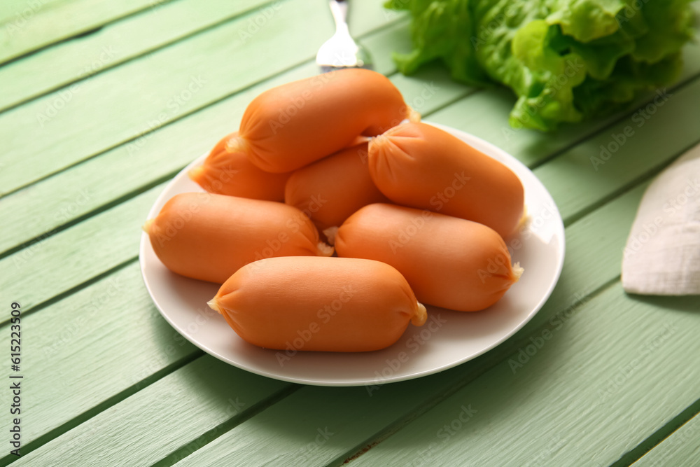 Plate of tasty boiled sausages and lettuce on green wooden background