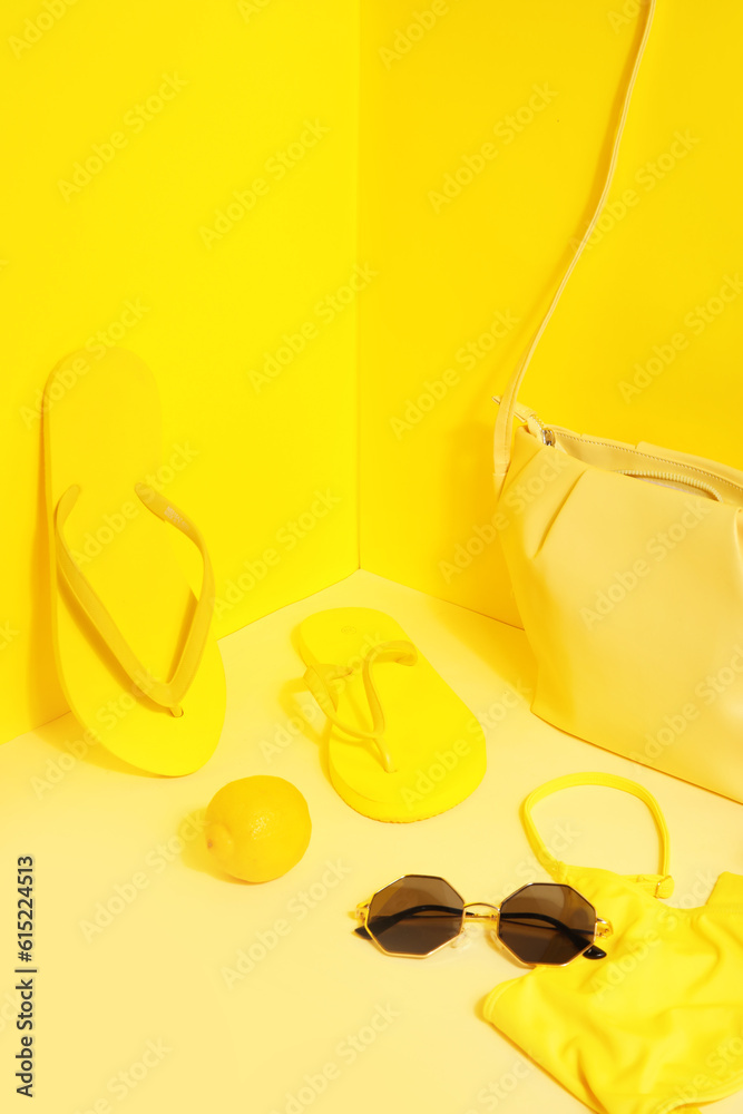 Flip flops with swimsuit, sunglasses and bag on yellow background