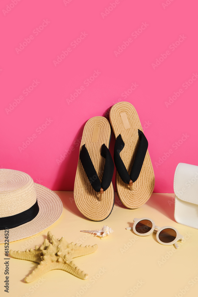 Flip flops with sunglasses, bag and wicker hat near pink wall