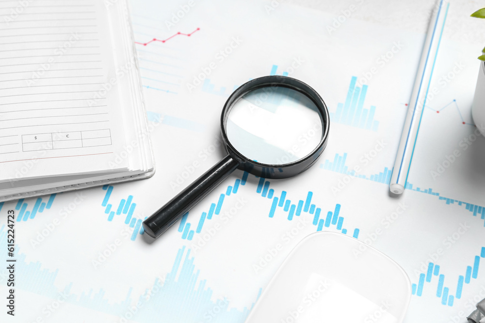 Magnifier with business charts on white table in office