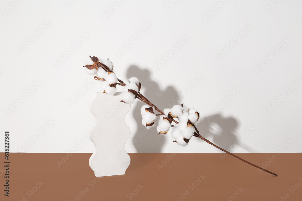 Cotton twig and stand on brown table near white wall