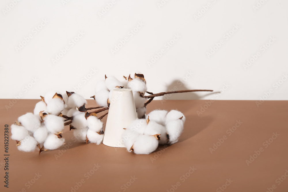 Cotton twig and cylinder stand on brown table near white wall