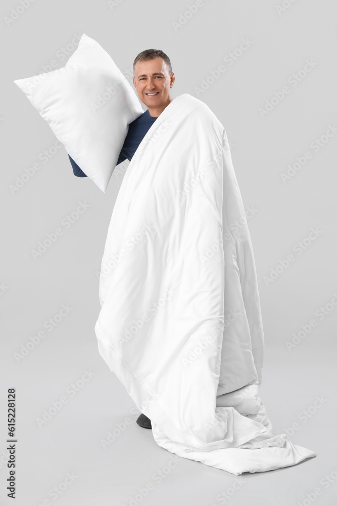 Mature man with soft pillow and blanket on grey background