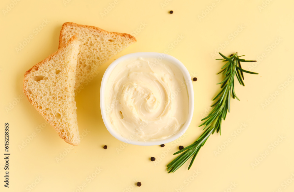 Bowl with tasty cream cheese and bread on yellow background