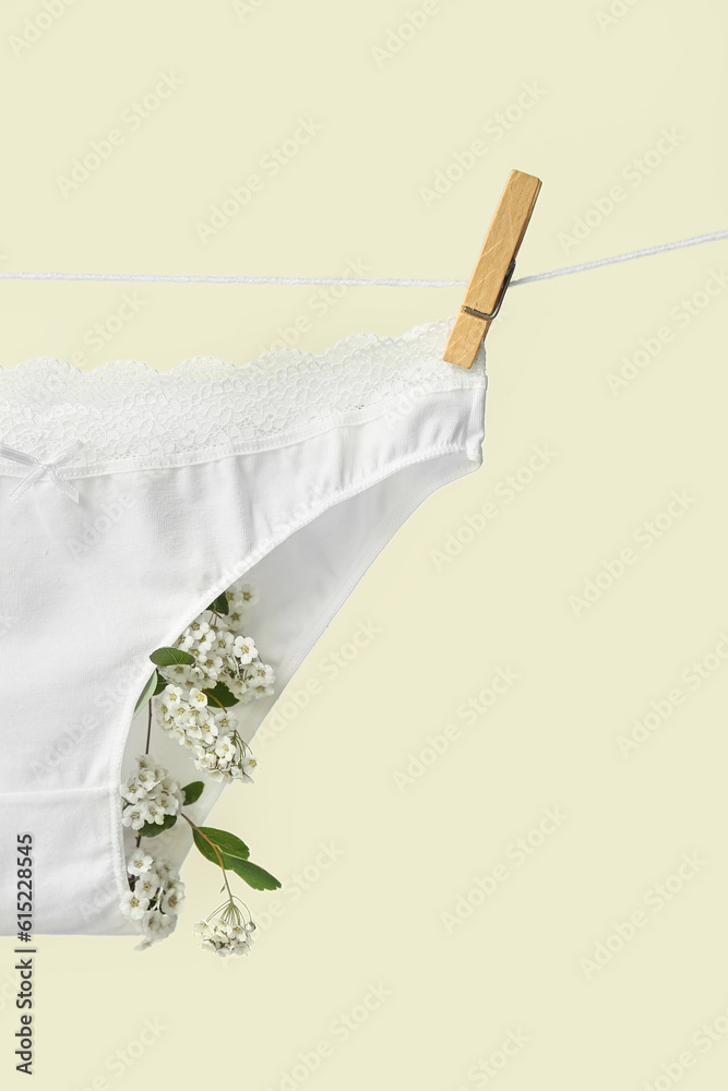 Female panties with blooming plant branches hanging on rope against light background, closeup