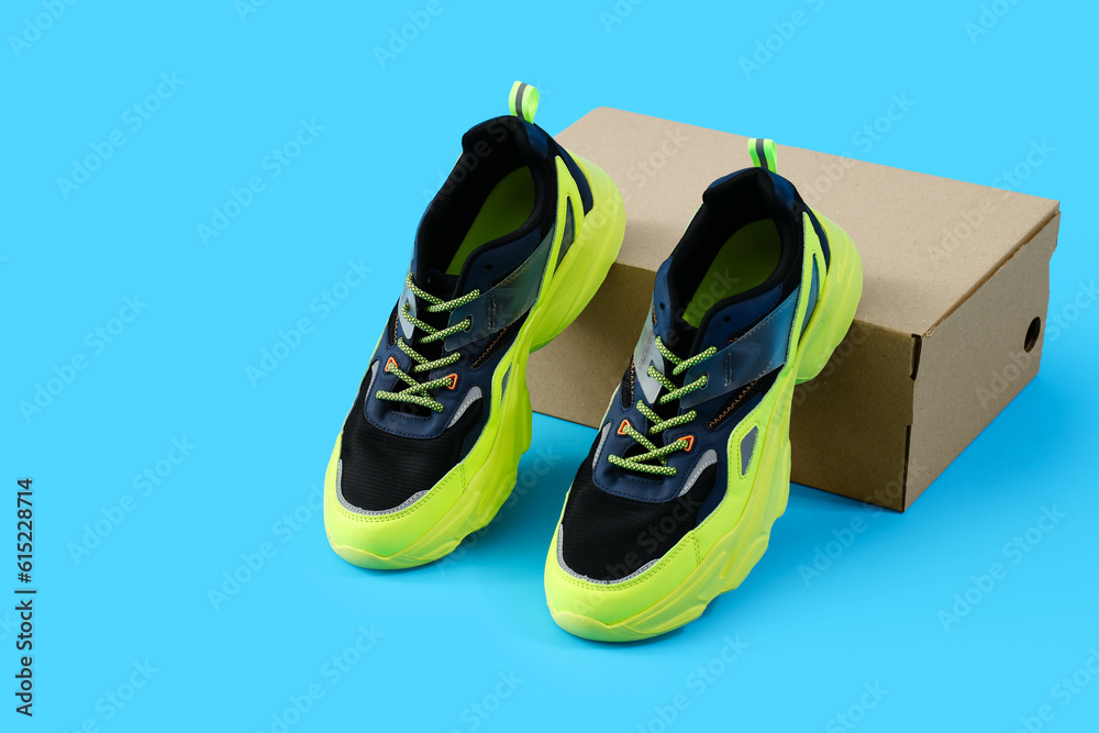 Cardboard box with stylish sneakers on blue background