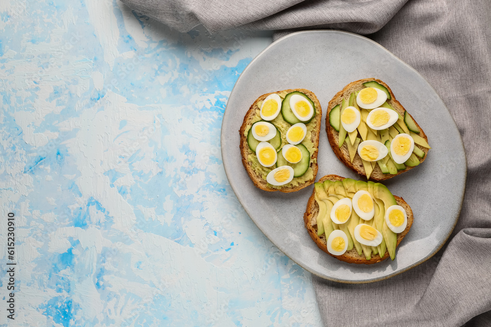 Tasty toasts with quail eggs, avocado and cucumber on light blue background