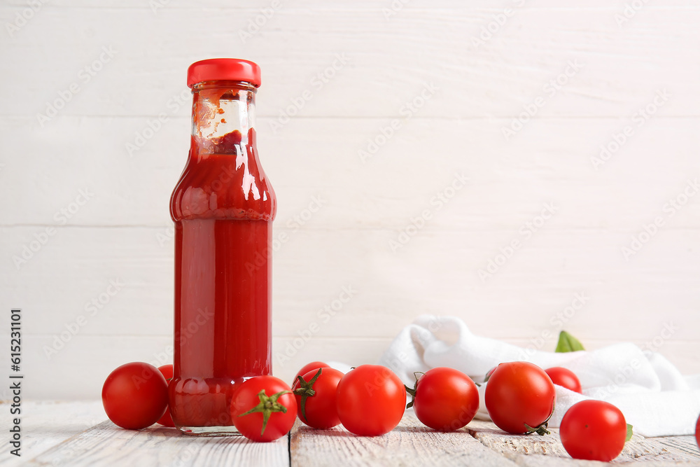 Glass bottle of ketchup and tomatoes on white wooden background