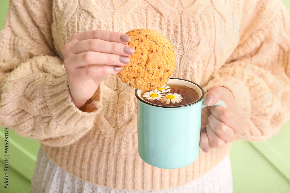 Beautiful young woman with cup of chamomile tea and cookie near green wall