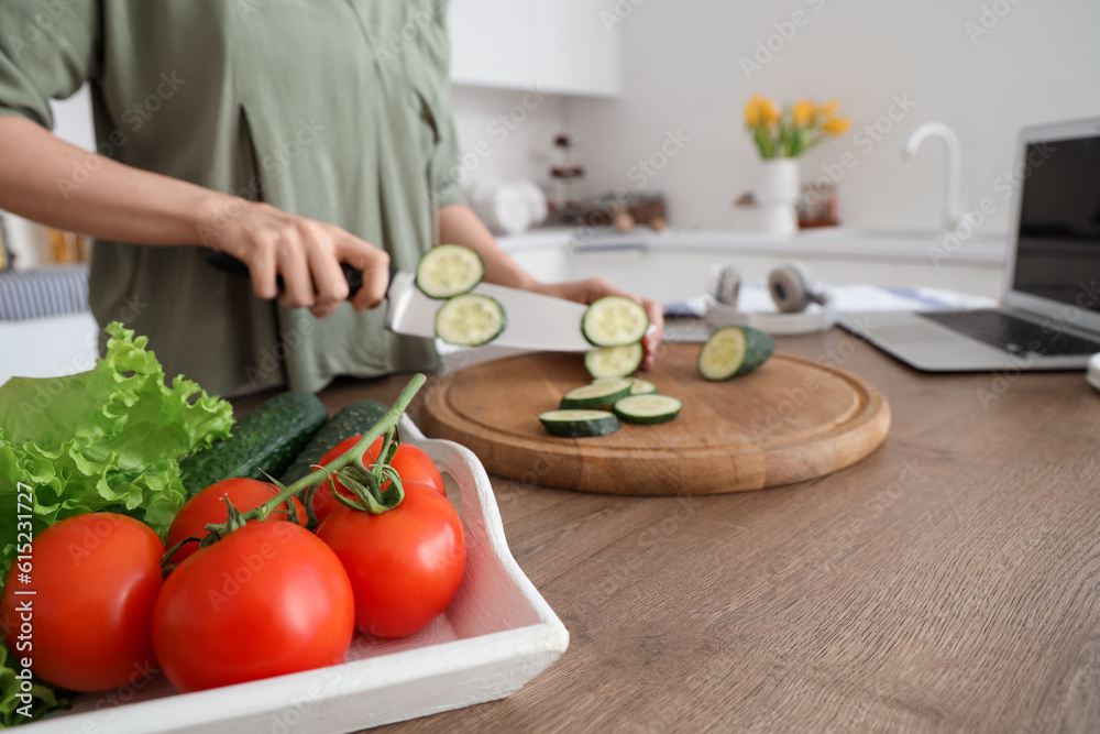 Woman cutting cucumber for salad on wooden table with vegetables