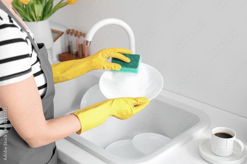 Woman in yellow rubber gloves washing plate with sponge in light kitchen