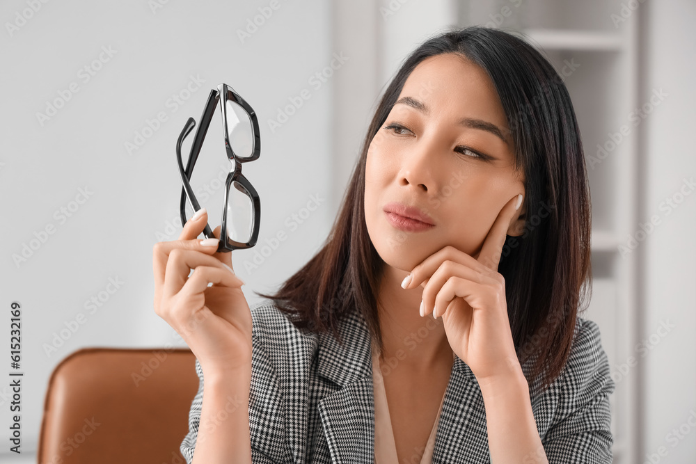 Thoughtful Asian businesswoman with stylish eyeglasses in office, closeup