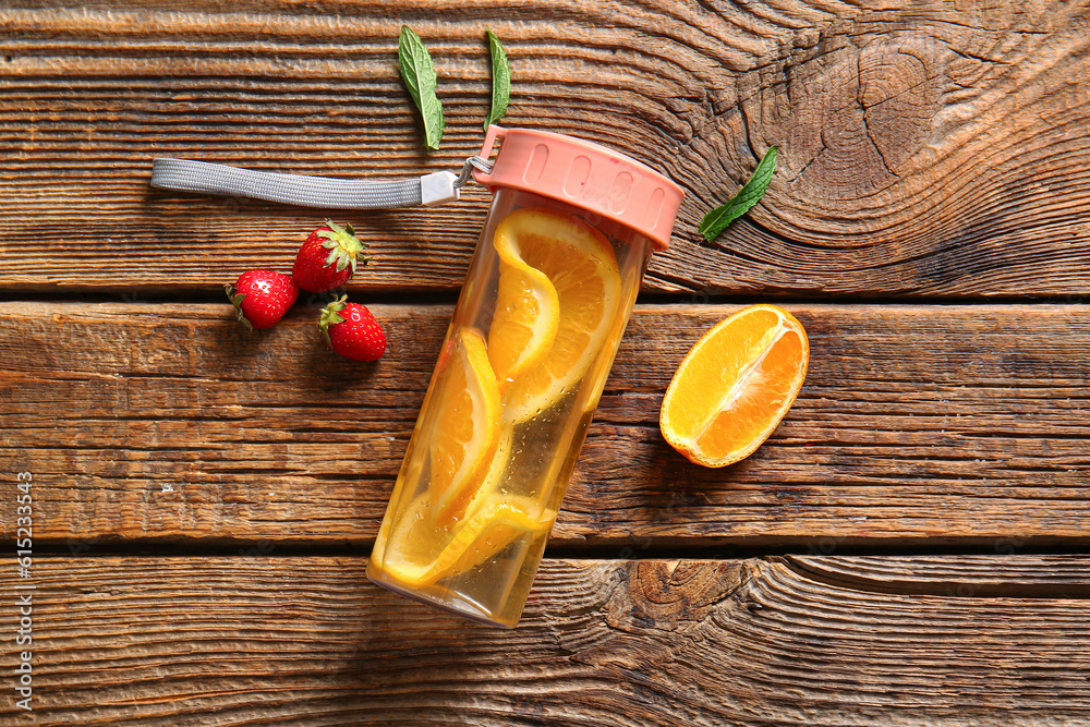 Sports bottle of infused water with orange slices on wooden background