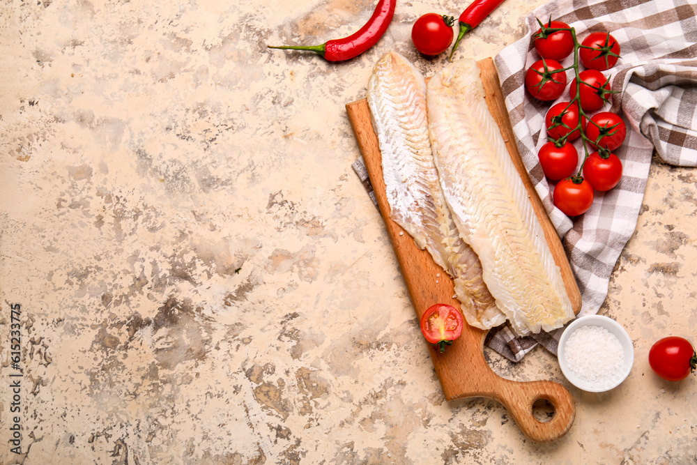 Wooden board with raw codfish fillet and tomatoes on beige background