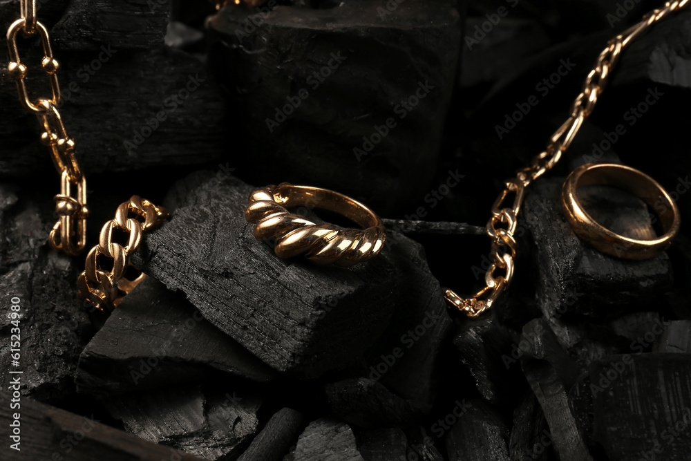 Beautiful chain bracelets and rings on black charcoal, closeup