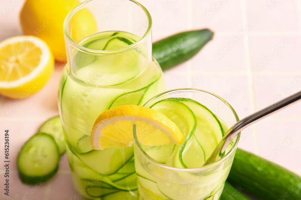 Glass and bottle of infused water with cucumber slices on pink tile table