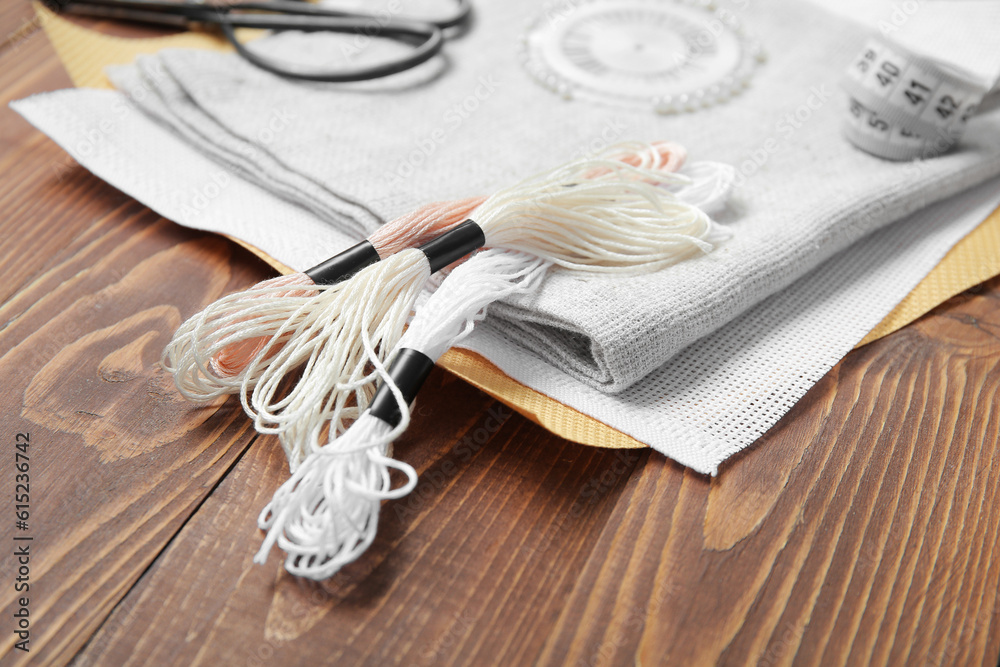 Different canvases with scissors, mouline threads and measuring tape on brown wooden background