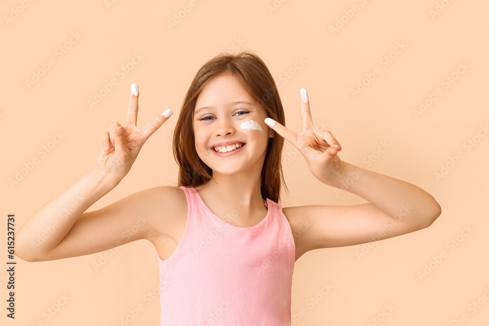 Little girl with sunscreen cream on her face showing victory gesture against beige background