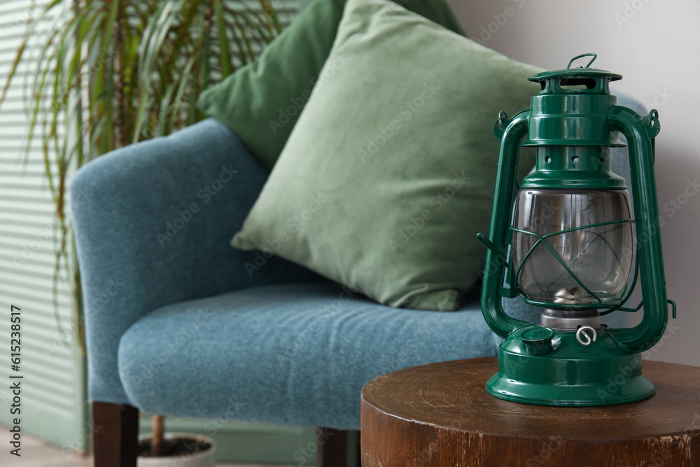 Vintage oil lamp on wooden stool near blue armchair, closeup