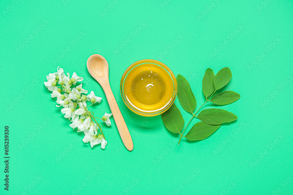 Bowl of honey with flowers of acacia and spoon on green background