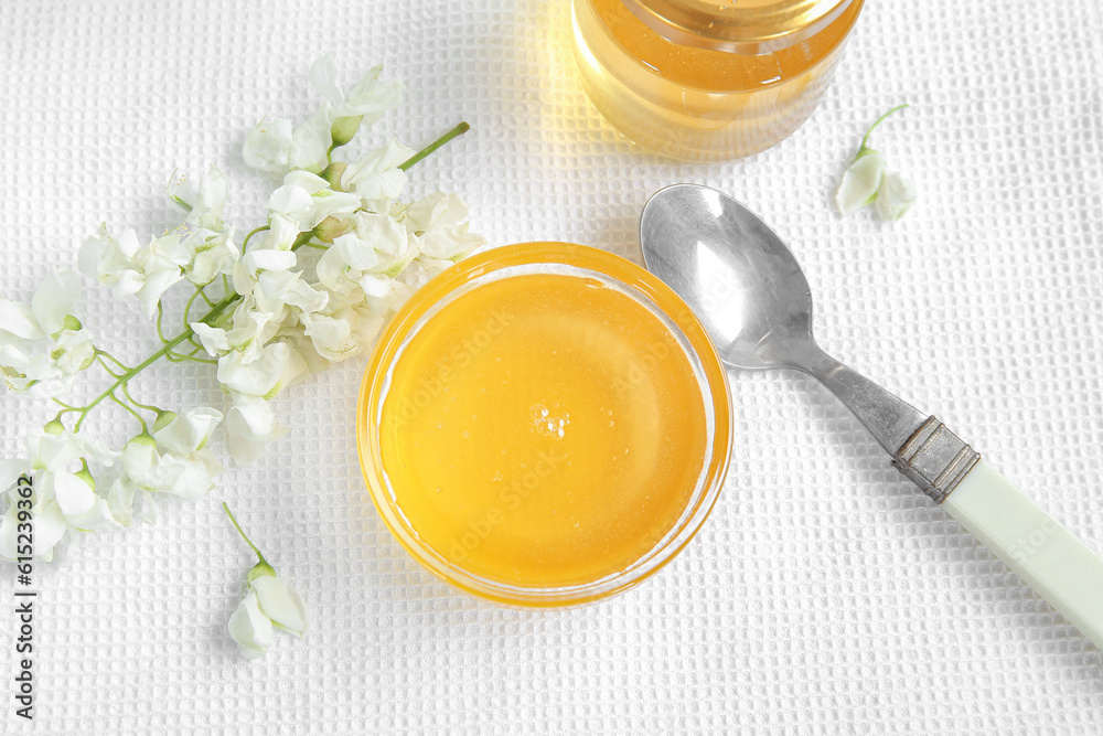 Bowl of honey with flowers of acacia on fabric background, closeup