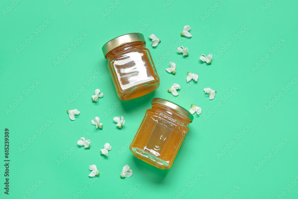 Jars of honey with flowers of acacia on green background