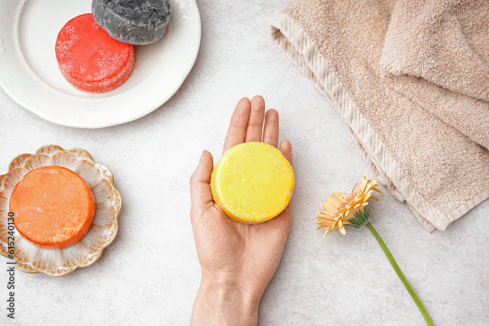 Female hand with handmade solid shampoo and calendula flower on light background