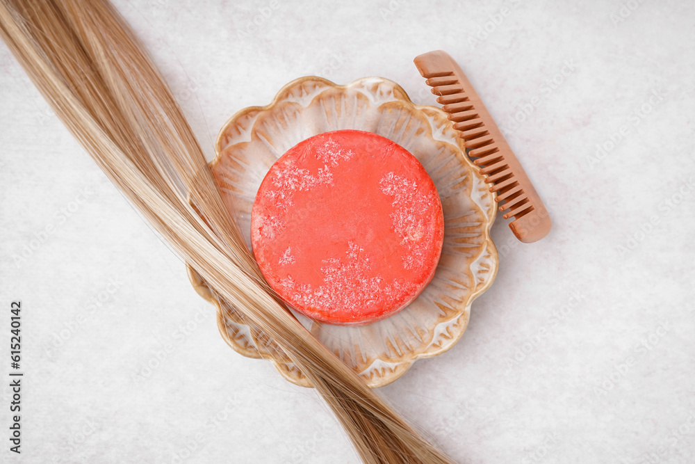 Stand with handmade solid shampoo, blonde hair and comb on light background