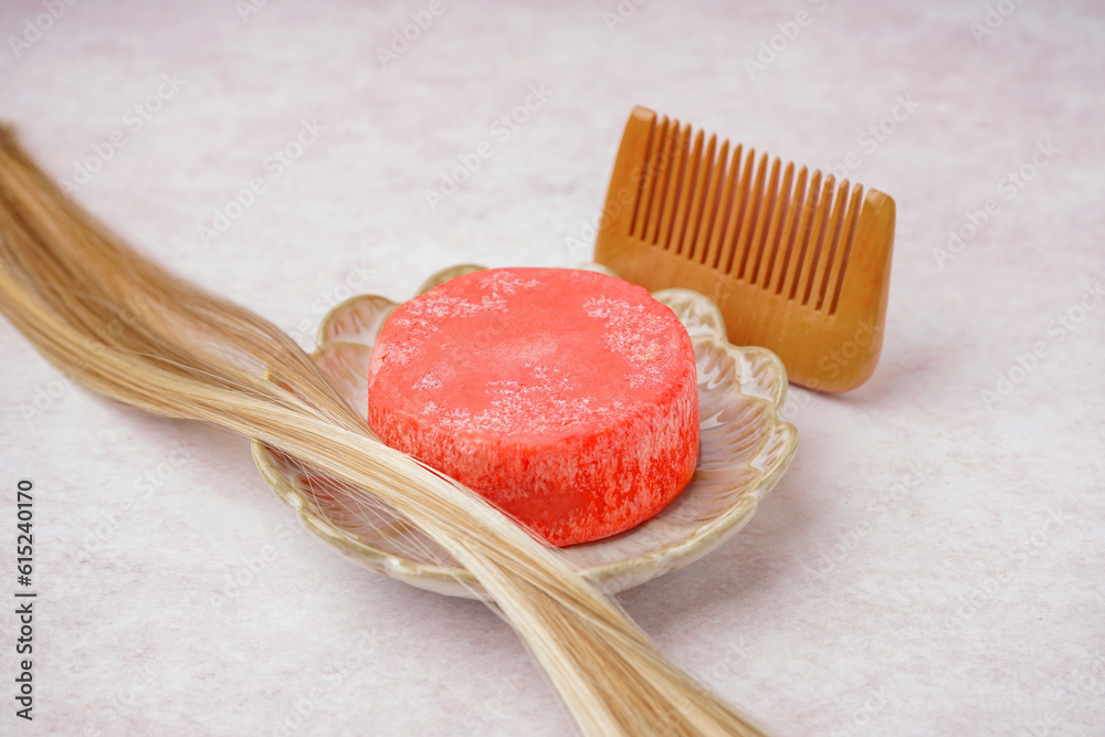 Stand with handmade solid shampoo, blonde hair and comb on light background, closeup