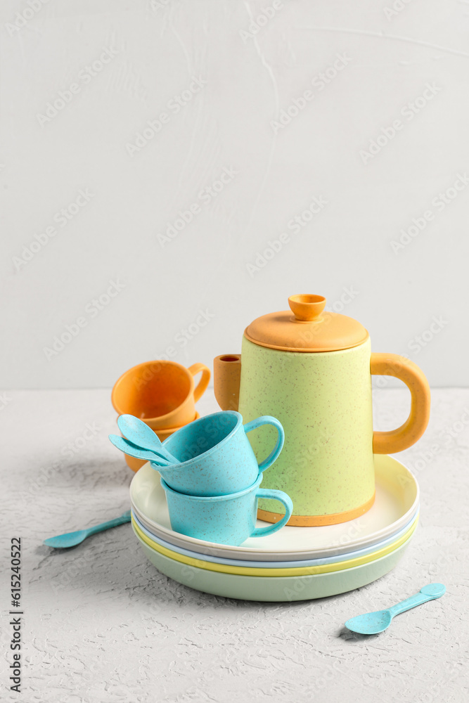 Plates with cups, teapot and spoons for baby on white table