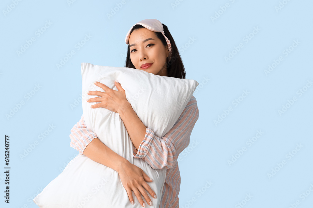 Beautiful Asian woman in pajamas with pillow on blue background