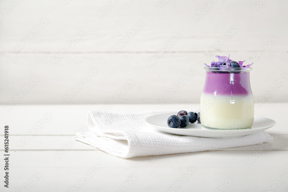 Glass of panna cotta with blueberry and beautiful hydrangea flowers on white wooden table