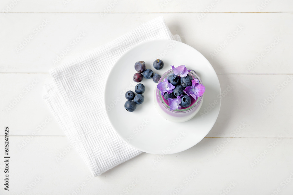 Glass of panna cotta with blueberry and beautiful hydrangea flowers on white wooden table