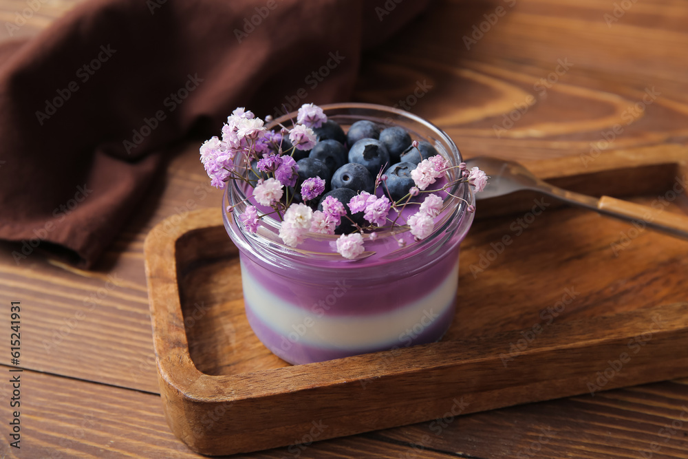 Glass of panna cotta with blueberry and beautiful gypsophila flowers on wooden background