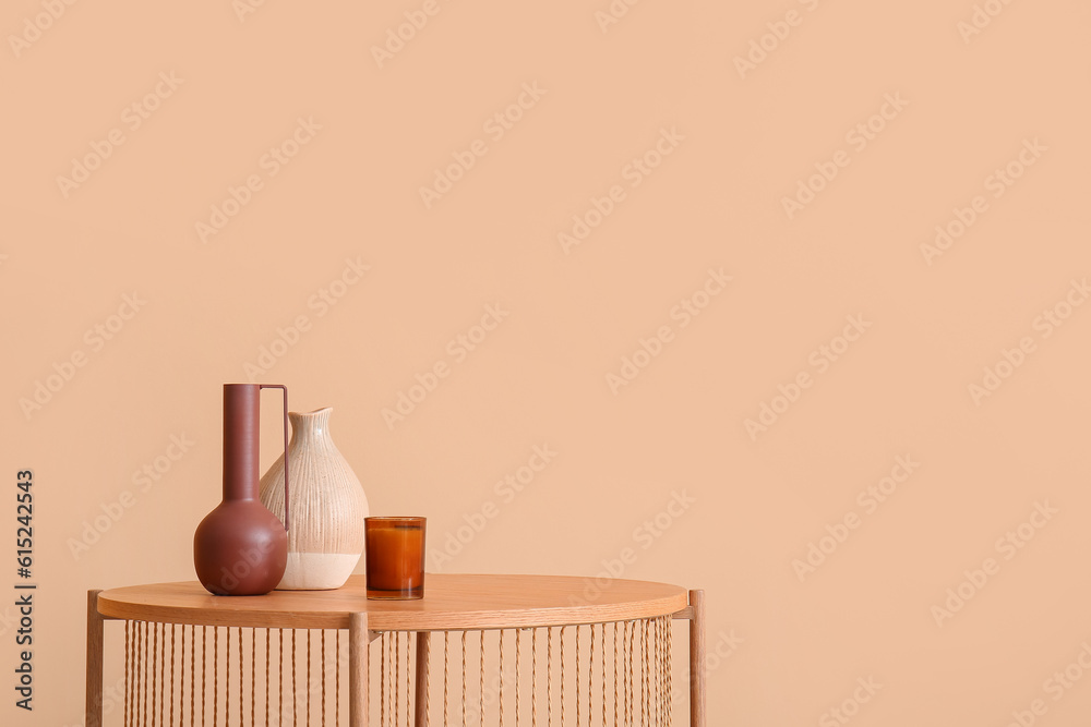 Wooden coffee table with empty vases and candle near beige wall