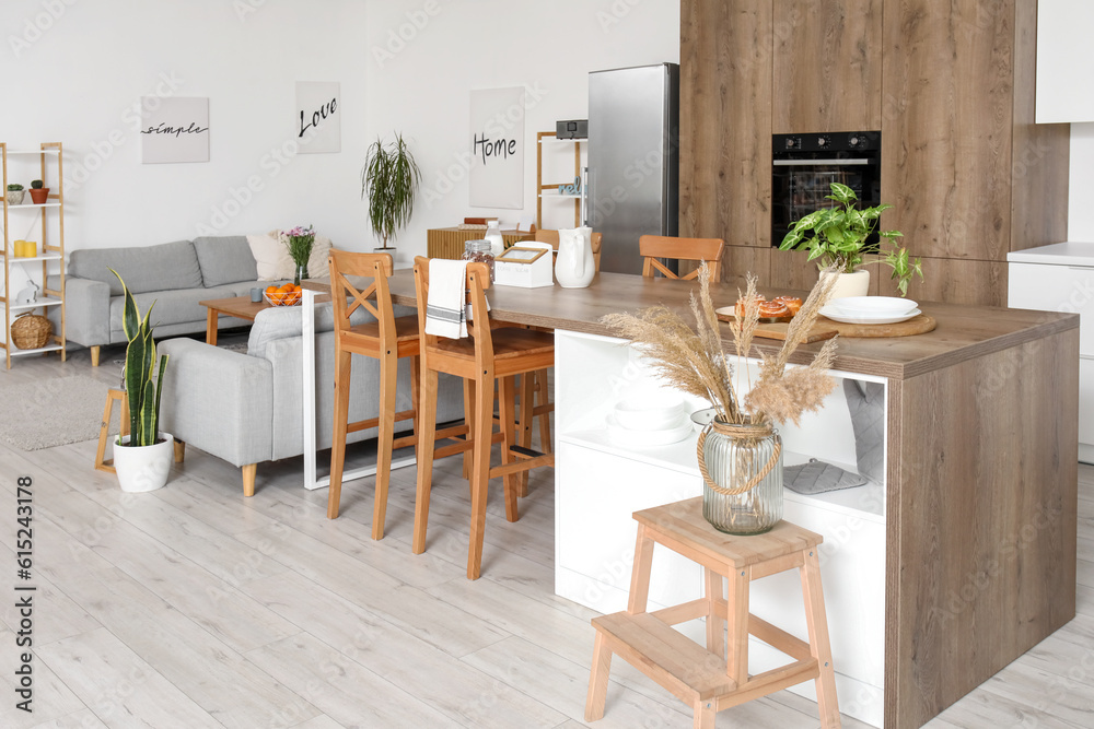 Interior of light open plan kitchen with island table and grey sofas