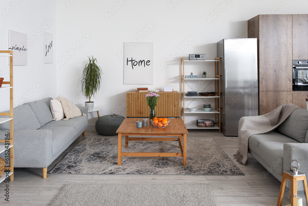 Interior of light open plan kitchen with fridge and grey sofas